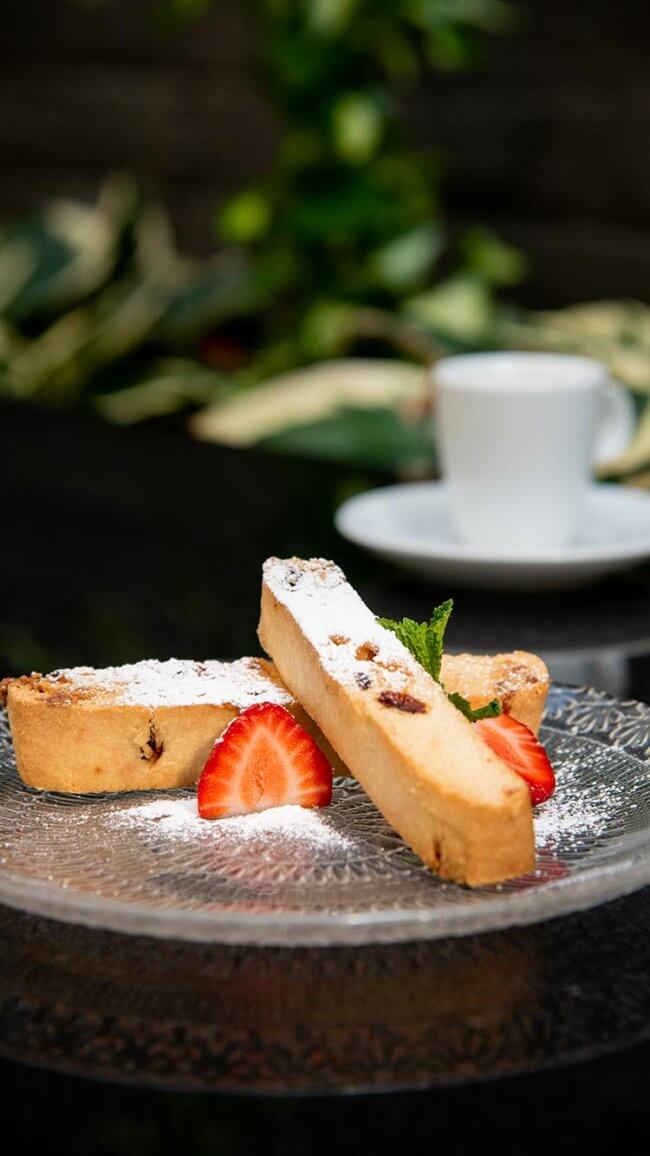 Biscotti dusted with powdered sugar, served with fresh strawberry slices and mint.