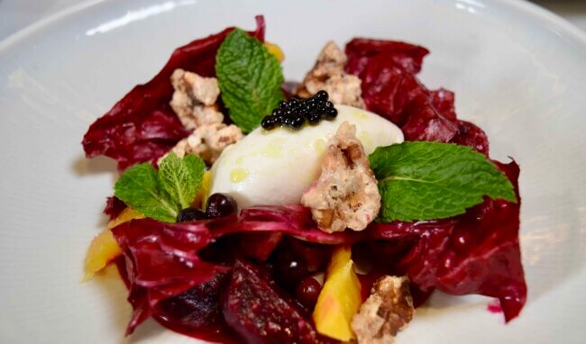 Fine dining dish featuring burrata topped with caviar, radicchio leaves, candied walnuts, and fresh mint.