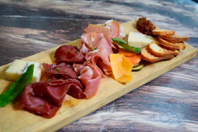 Cured meats and cheese assortment with crostini, pickled vegetables, and relish on a wooden serving board.