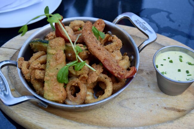 Crispy fried calamari and vegetables served in a metal skillet with a creamy dipping sauce.