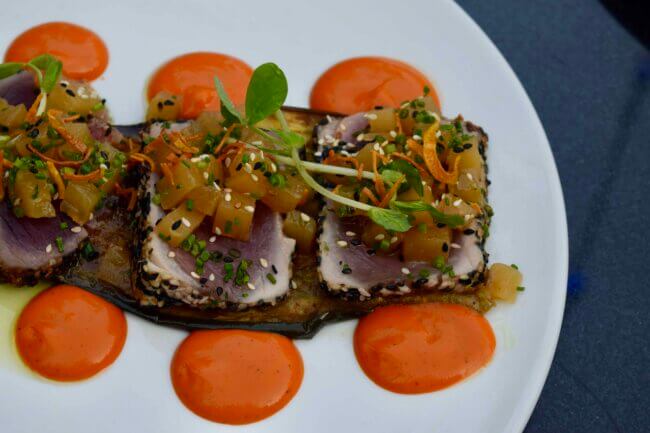 Seared tuna with vegetable topping and spicy red sauce dots, served as a modern plated dish.