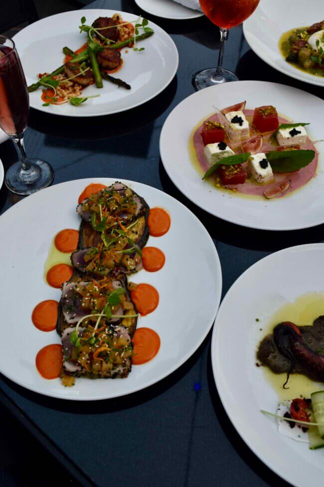 Variety of fine dining appetizers and entrées served on white plates with wine glasses.