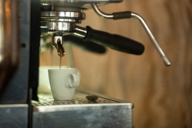 Fresh espresso pouring from a professional espresso machine into a small white cup