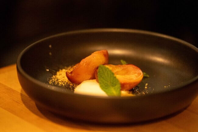 Gourmet dessert featuring roasted peaches, cream, and mint garnish served in a black bowl