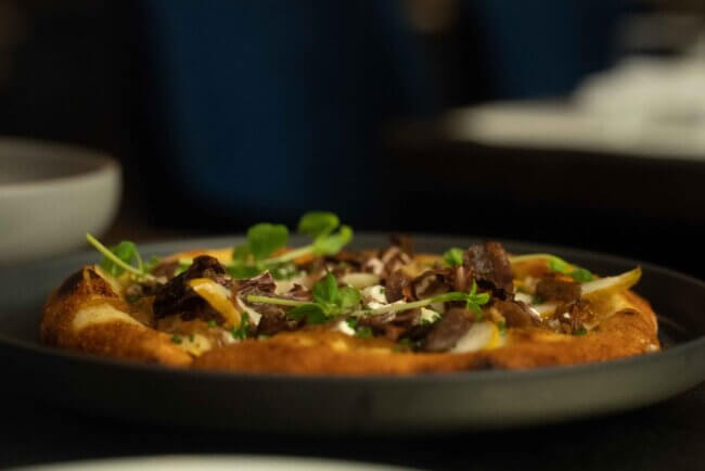 A chef preparing food in an open kitchen, with steam rising and culinary tools visible.