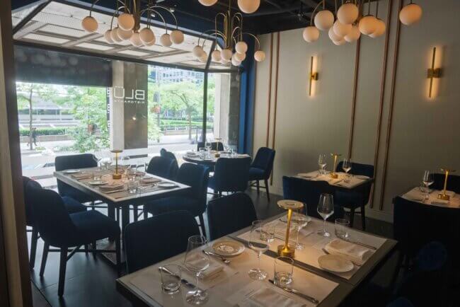 Chic restaurant interior with tables set for dining and large windows.