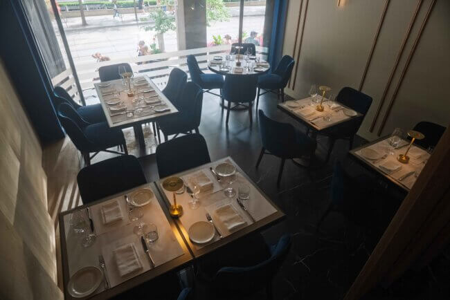 Stylish restaurant interior with multiple tables set for dining and large windows.