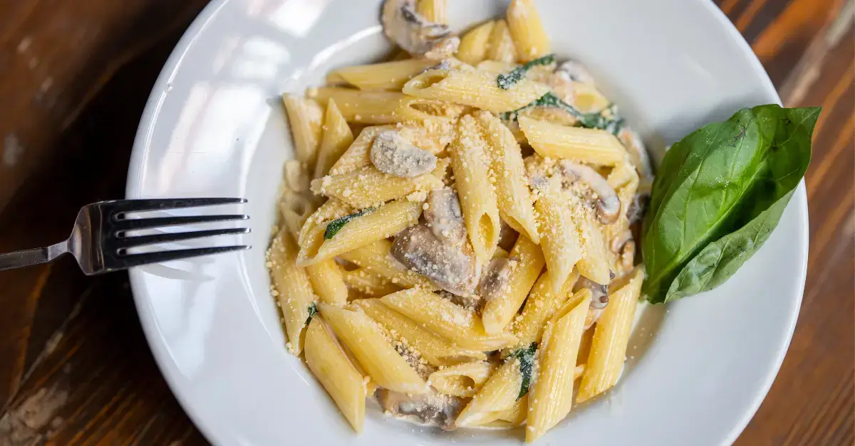 Plate of creamy penne pasta with mushrooms, Parmesan cheese, and basil, served in an Italian restaurant in downtown Toronto.
