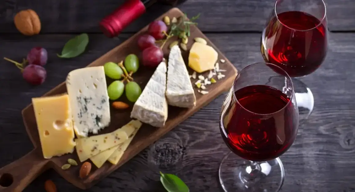 Selection of Italian cheeses with grapes, nuts, and two glasses of red wine, a perfect pairing for authentic Italian dining.