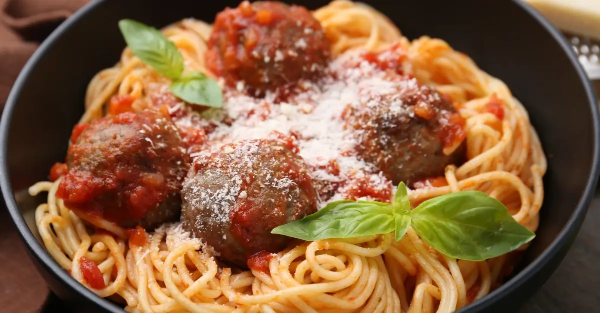 Bowl of spaghetti with meatballs in tomato sauce topped with Parmesan cheese and basil, representing Italian-American food tradition.